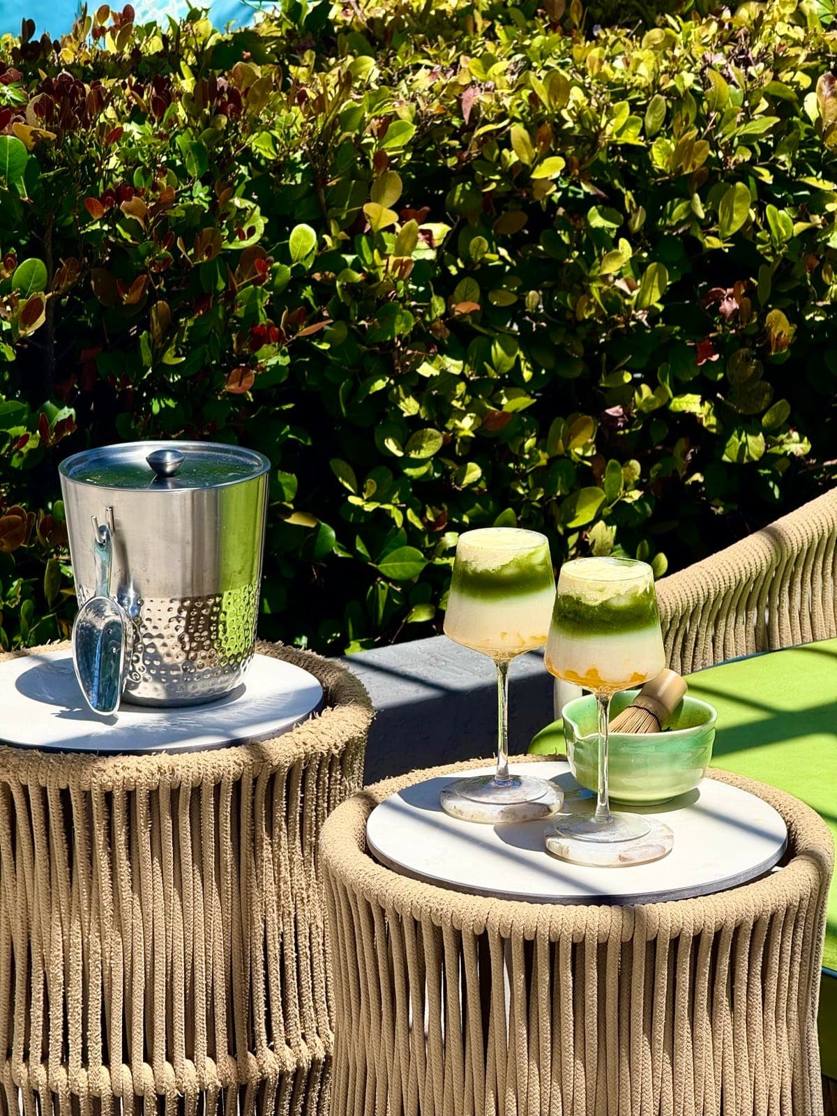 Two layered Azure matcha drinks on a poolside table beside a silver ice bucket