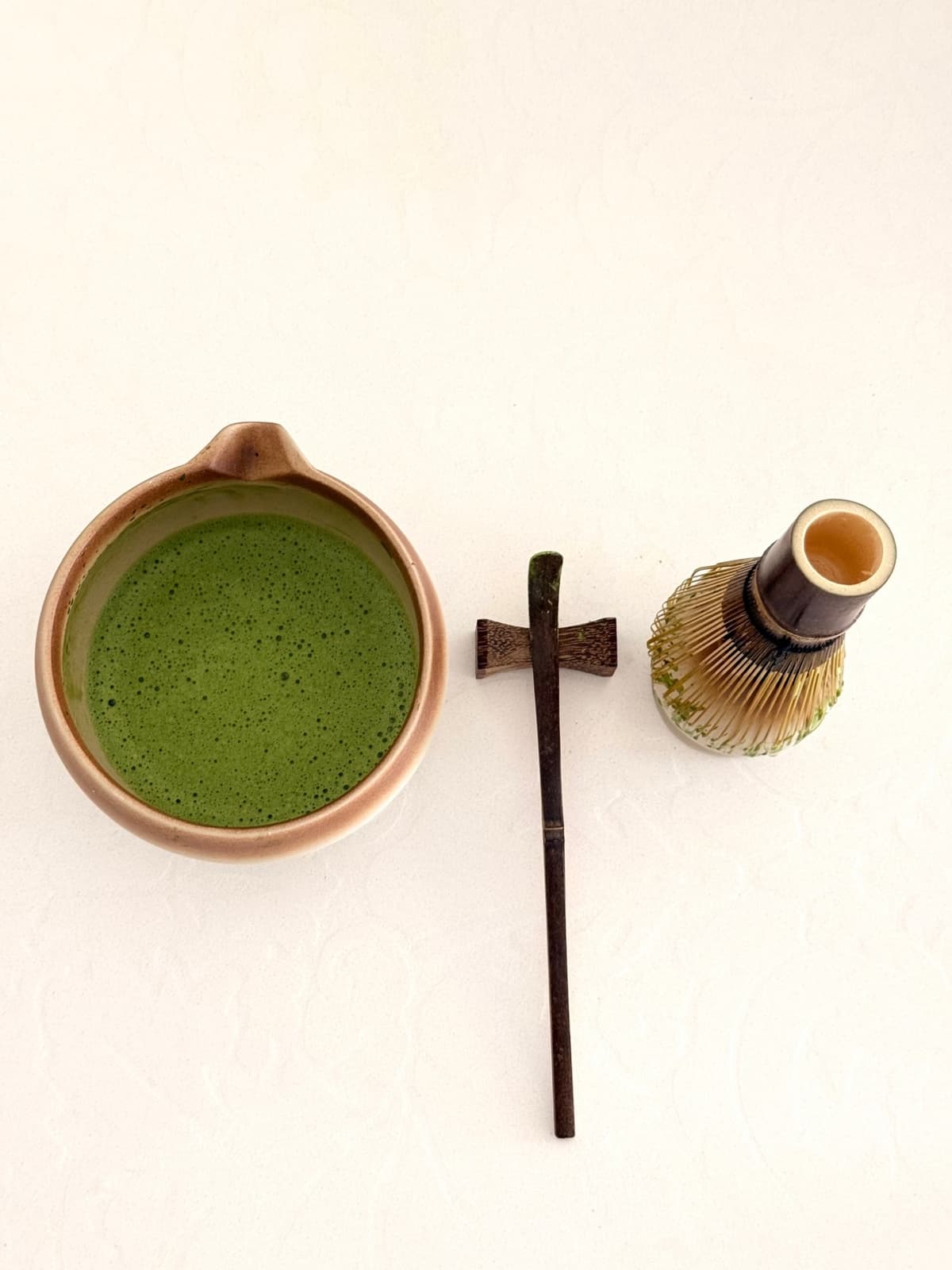A bowl of whisked matcha beside a bamboo scoop and whisk
